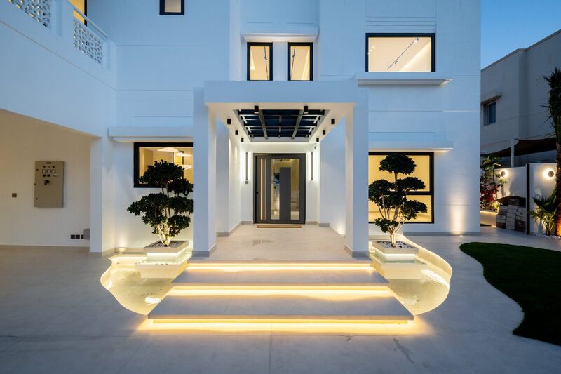 The Meadows villa front entrance after renovation — new all-white façade, pivot door and illuminated steps